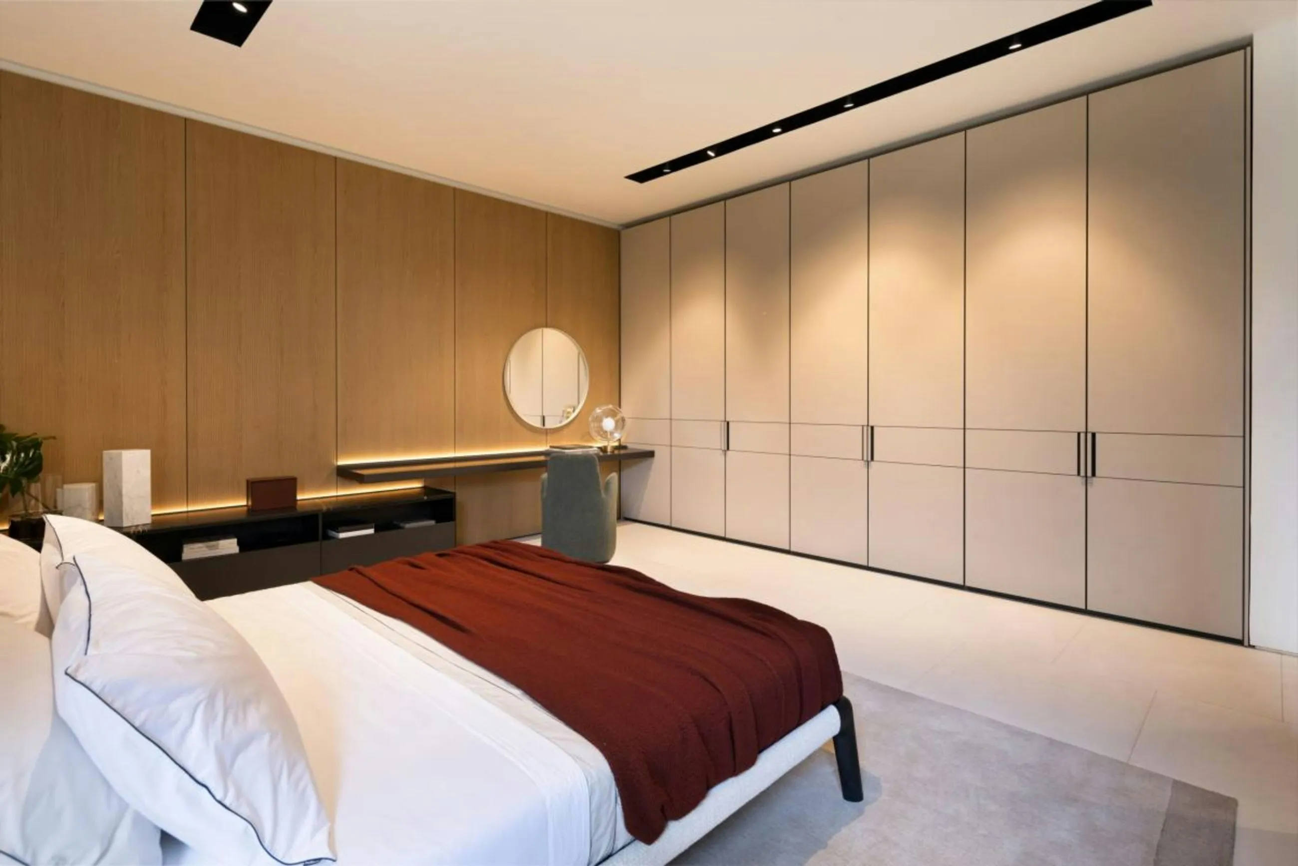 Quarto com parede inteira de guarda-roupa em tom areia e painel de madeira com penteadeira.
